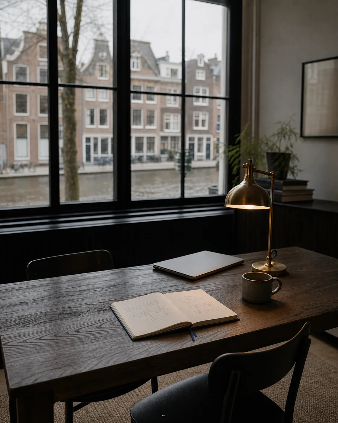 Illustration of a desk by a canal window, with a notebook of page sketches and a brass lamp